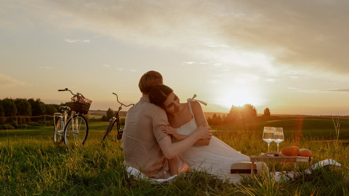 Couple hugging each other on a picnic blanket in a sunny grassy park on a budget date