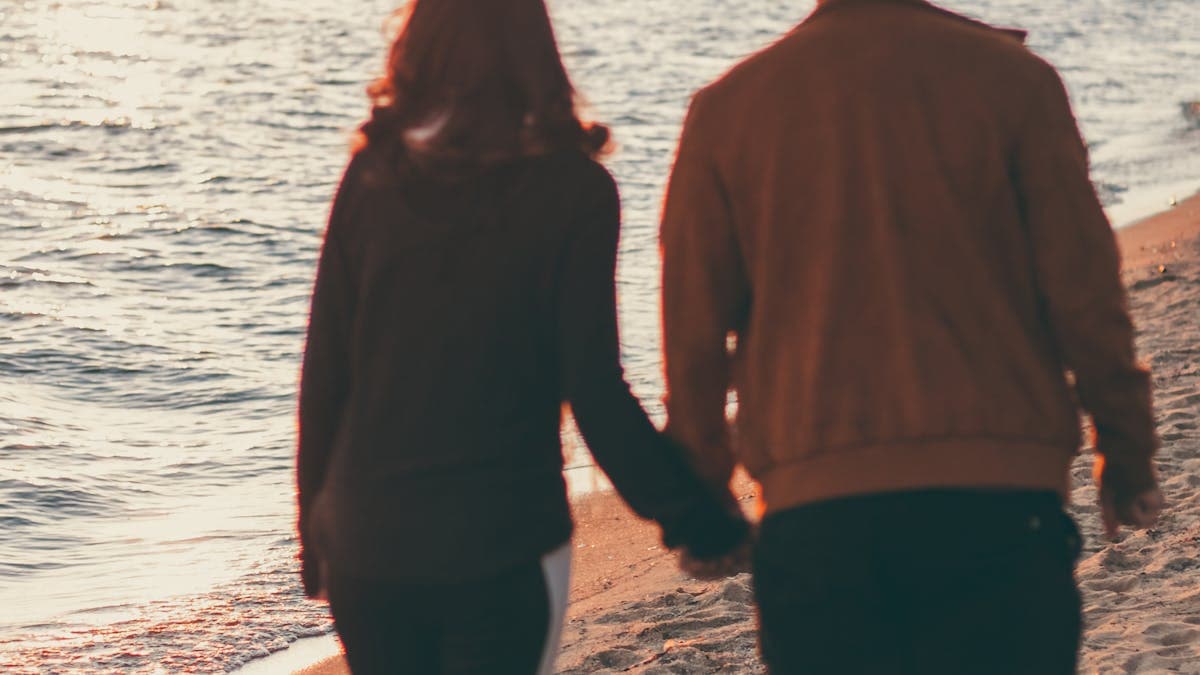 Newlywed couple holding hands while walking on a Florida beach at sunset during their honeymoon