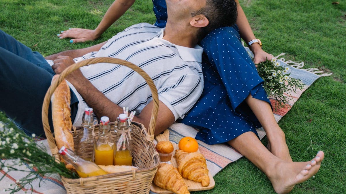 Couple relaxing together on a picnic blanket in a sunlit park, enjoying a romantic outdoor afternoon