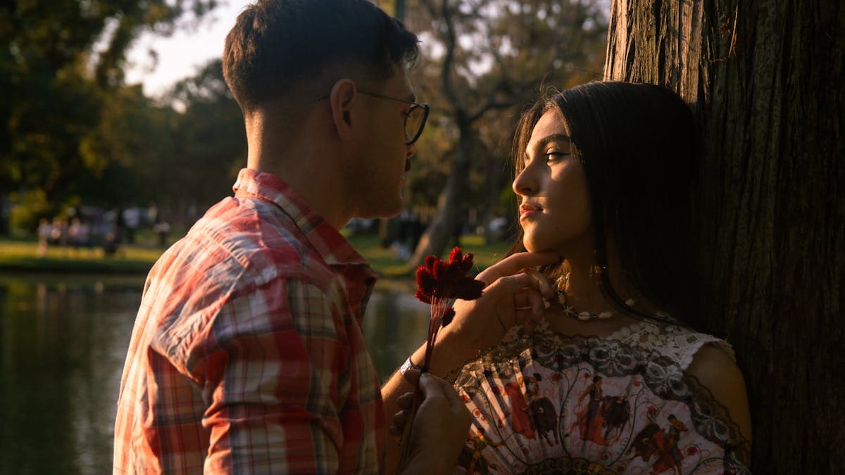 Romantic couple by a lake at golden hour, silhouetted against a warm glowing sunset sky